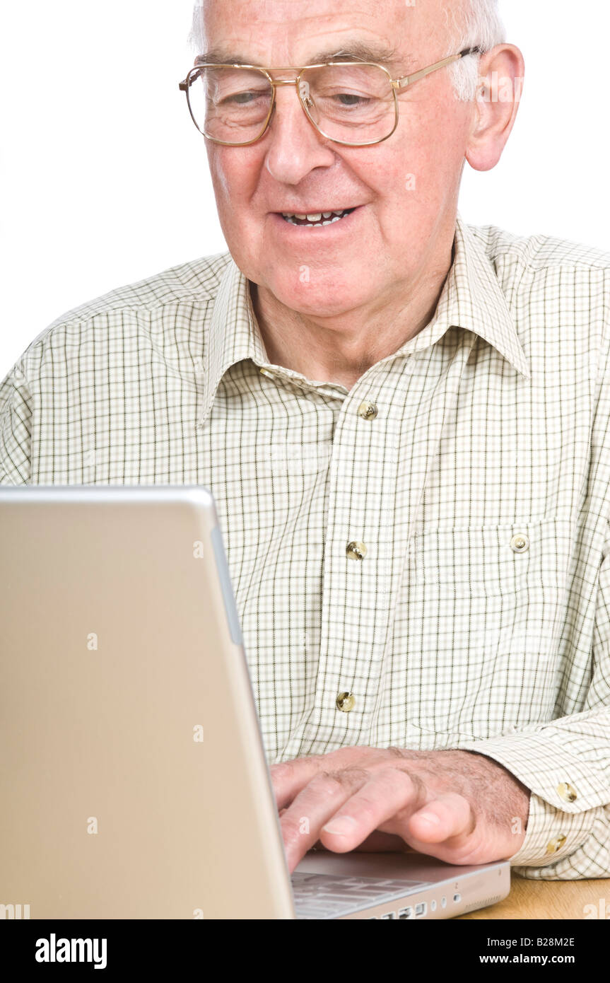 Un uomo anziano a una scrivania guardando un lap top computer schermo e sorridente contro un bianco puro (255) dello sfondo. Foto Stock