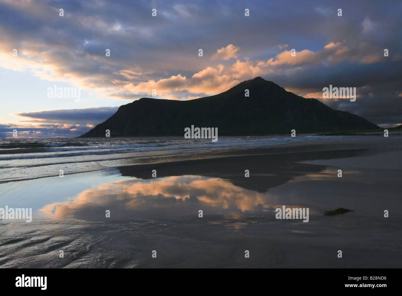 Una riflessione di lontane colline nella spiaggia bagnata con drammatica Nuvole rosa derivanti dalla bassa raggi del sole di mezzanotte Foto Stock