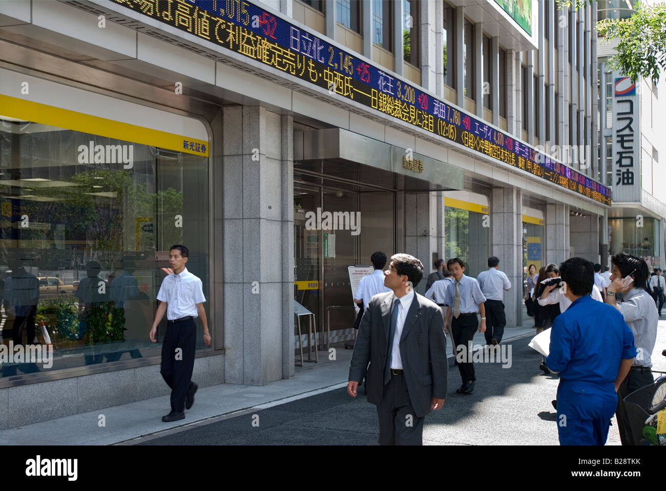 Imprenditori passando a Tokyo società di titoli mobiliari che visualizza le ultime mercato azionario cifre su un esterno di electronic Ticker tape Foto Stock