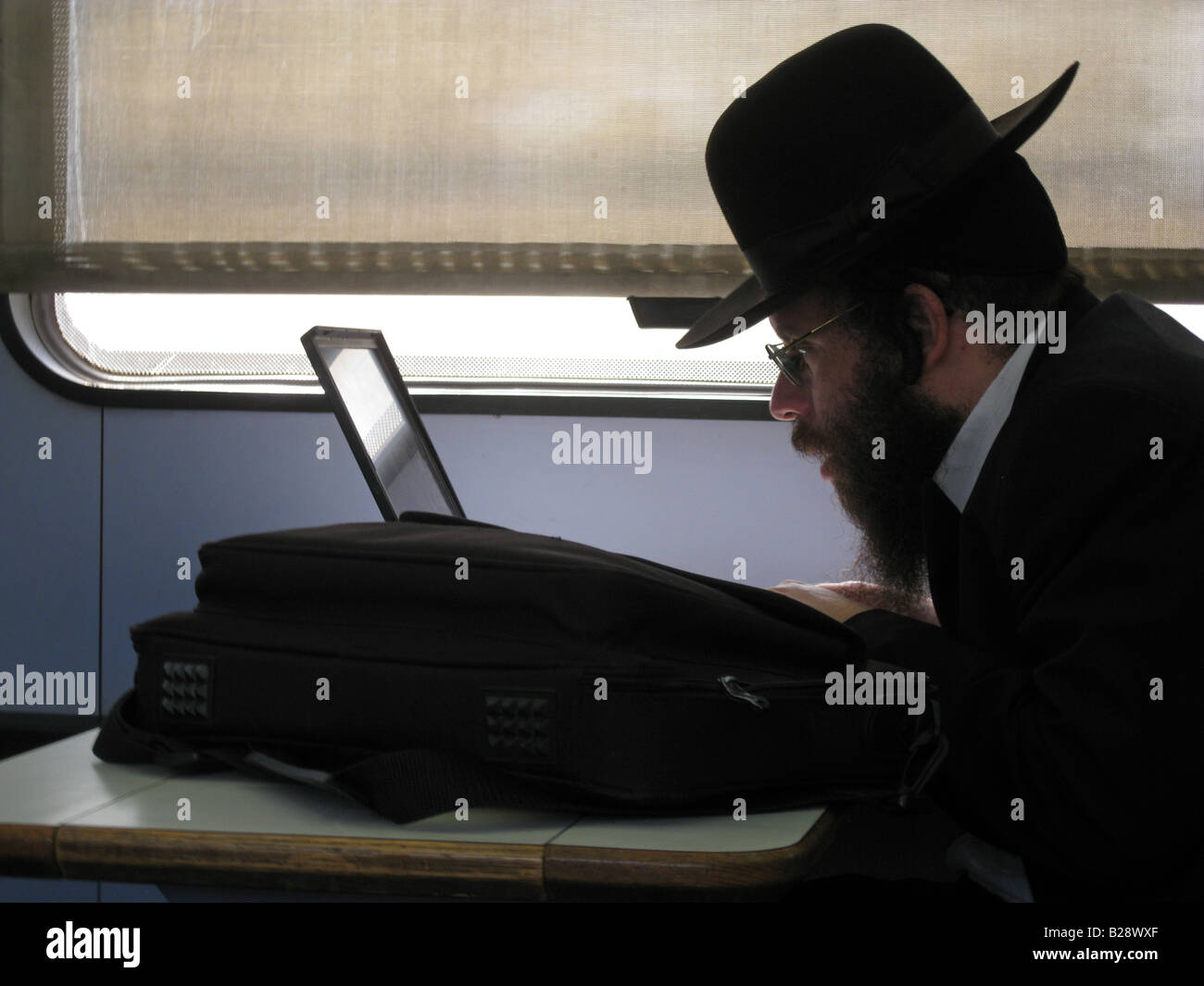 Ultra ortodosso passeggero ebraico con computer portatile seduto nella cabina del treno in Israele Foto Stock