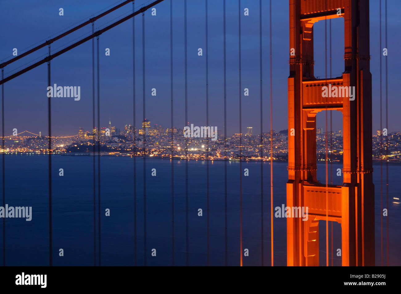 Skyline di San Francisco e il Bay Bridge illuminazione incorniciato da incandescente Golden Gate pilastro e cavi di acciaio Foto Stock