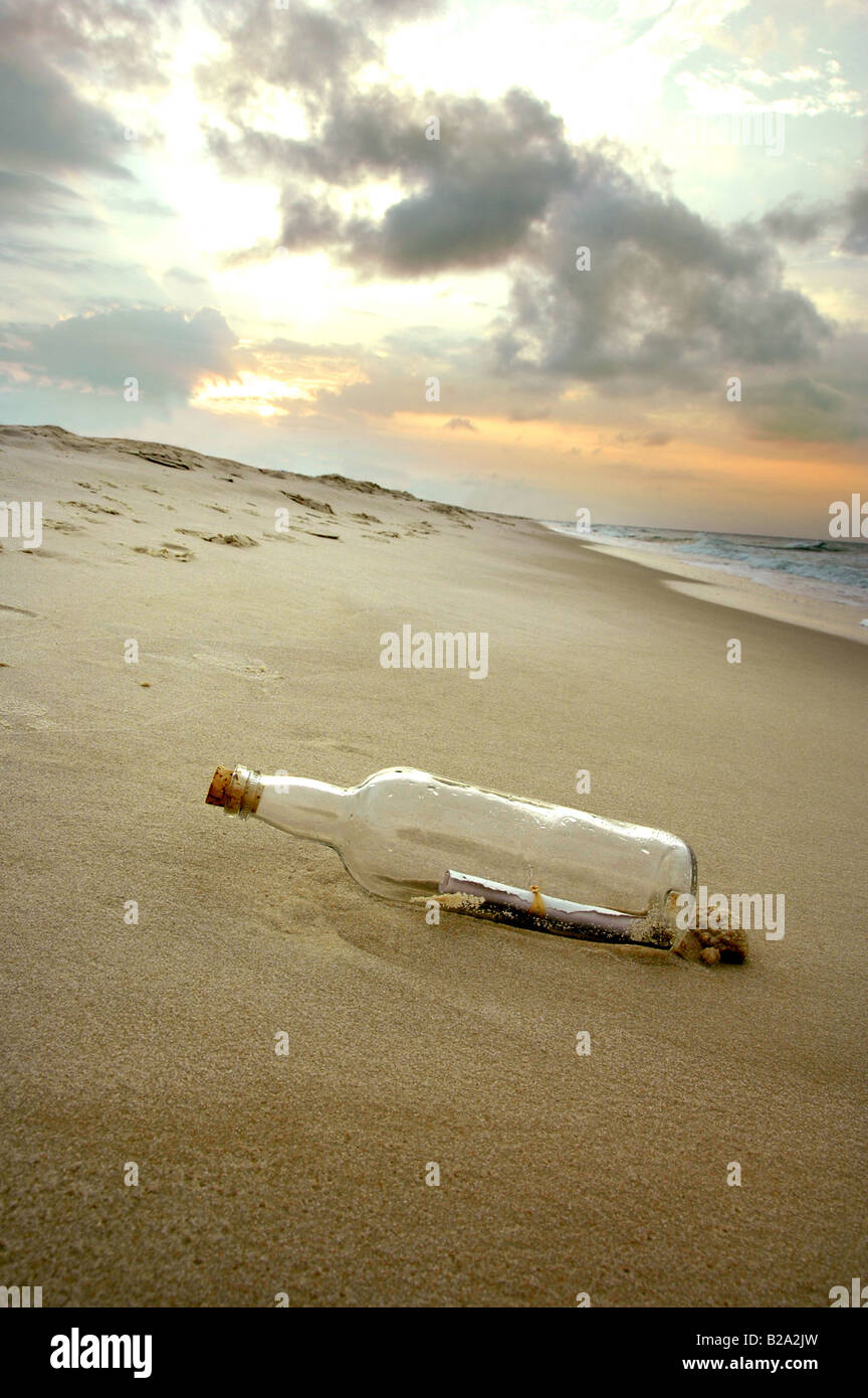 Un messaggio in bottiglia arenati su una riva deserta come il sole tramonta Foto Stock