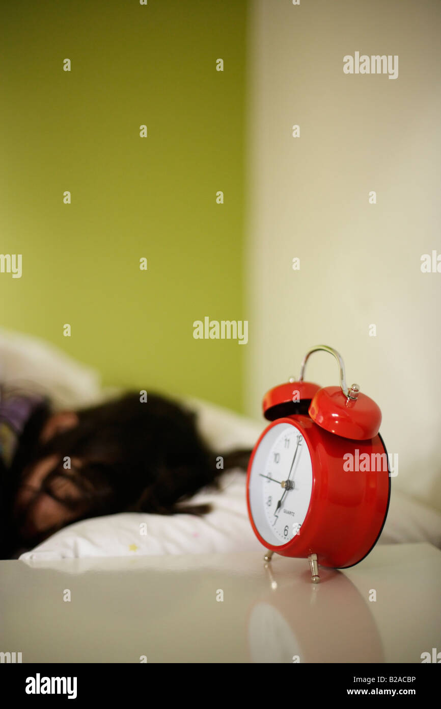 Ragazza di età compresa tra i cinque posti letto nel suo letto accanto a Colore rosso brillante sveglia razza mista inglese indiano Foto Stock