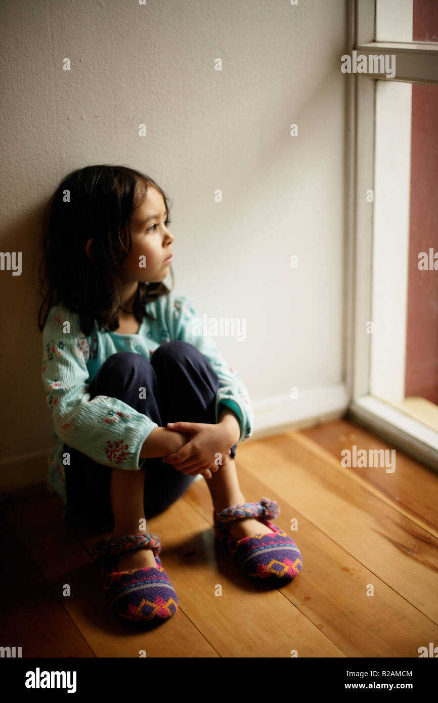 Ritratto di bambina all età di cinque anni seduto sul pavimento accanto alla finestra razza mista di etnia indiana e caucasico Foto Stock