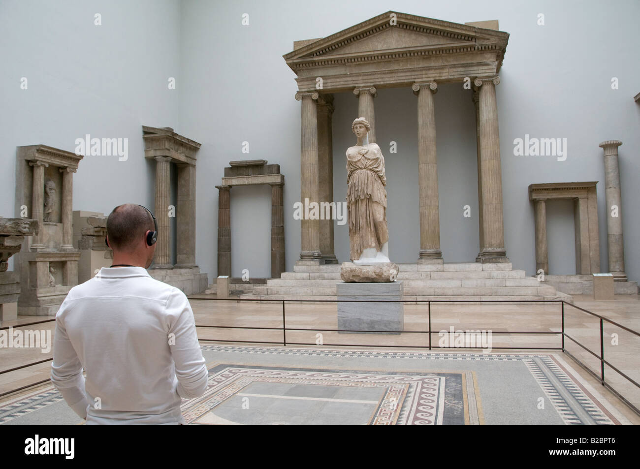 Un visitatore guardando il Greco antico reliquie e di indossare le cuffie per audio guida tour del sistema Nel Pergamon Museum in Museumsinsel isola Berlino Germania Foto Stock
