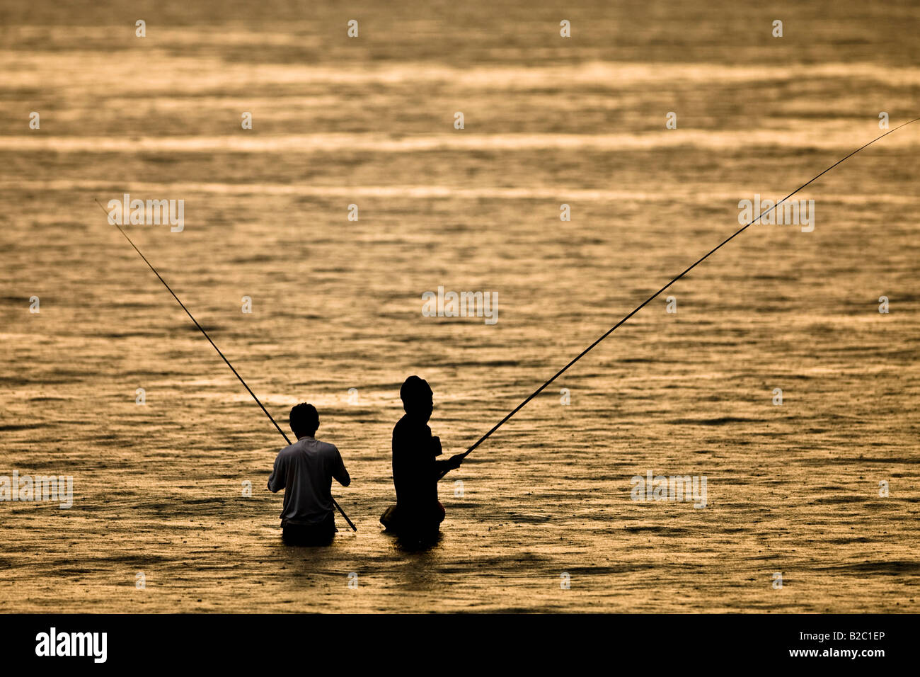 Due pescatori pesca al tramonto, stando in acqua sotto una leggera pioggia, Isola di Lombok, Indonesia, Asia Foto Stock