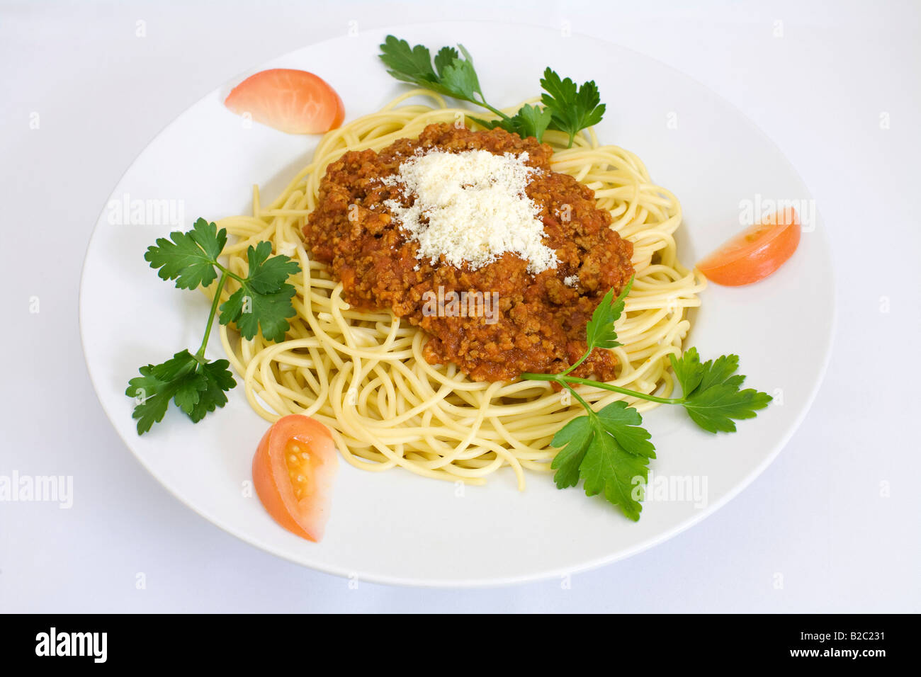 Spaghetti alla bolognese con formaggio parmigiano, guarnite con fette di pomodoro e prezzemolo a foglia piatta Foto Stock