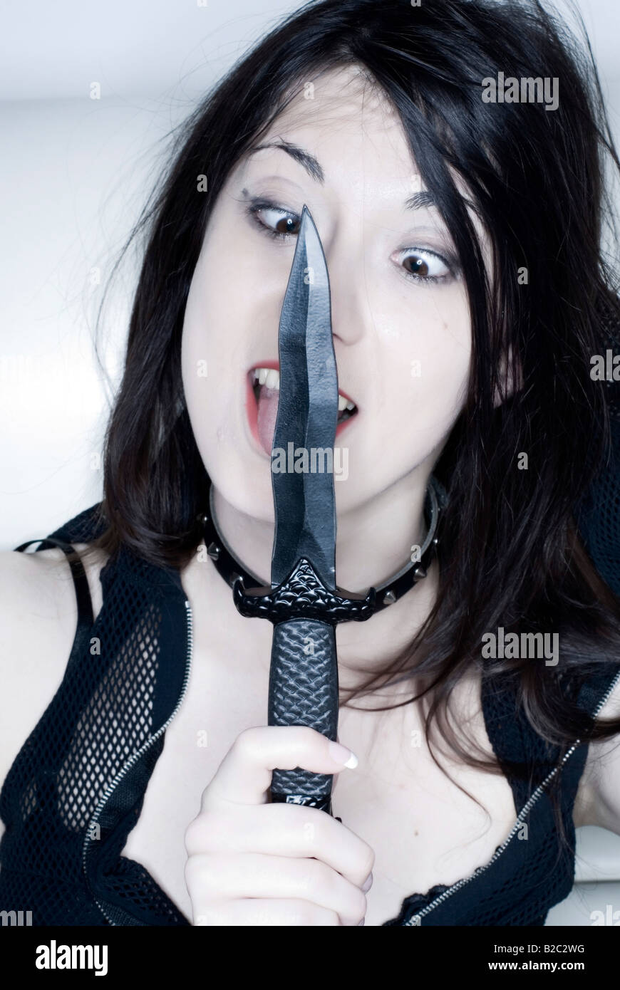 Giovane donna gotico leccare un coltello Foto Stock