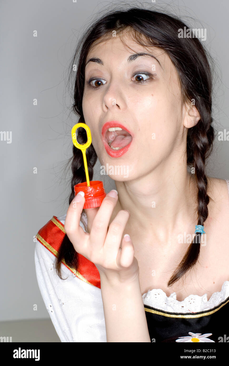 Giovane donna con due trecce che indossa un vestito con grembiule, rendendo le bolle di sapone Foto Stock