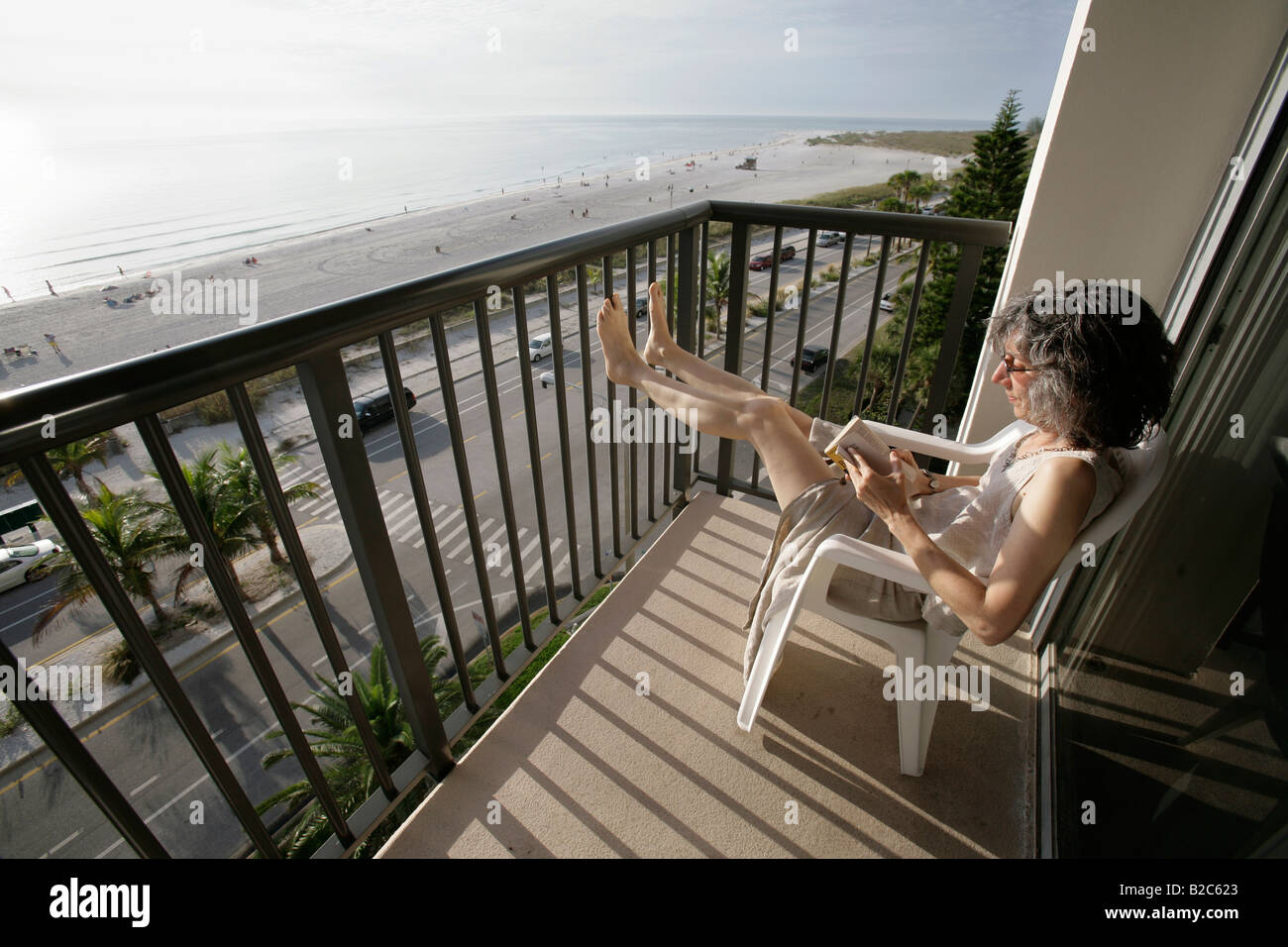 Una donna legge seduto su di una terrazza che si affaccia sulla spiaggia di Fort Myers e sulla costa del Golfo della Florida Foto Stock