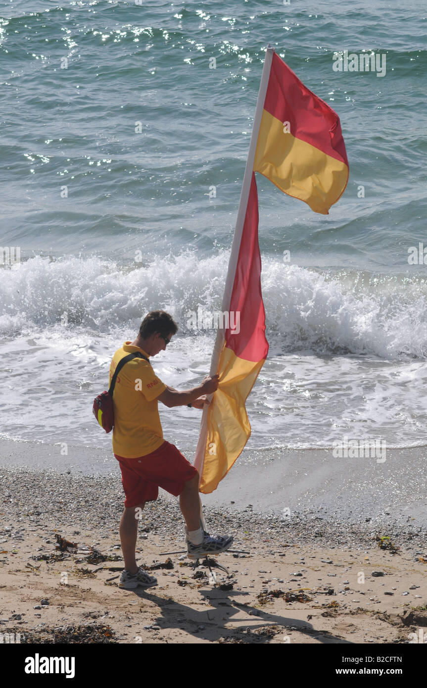 Un bagnino di salvataggio su un falmouth beach erige un flag di sicurezza Foto Stock