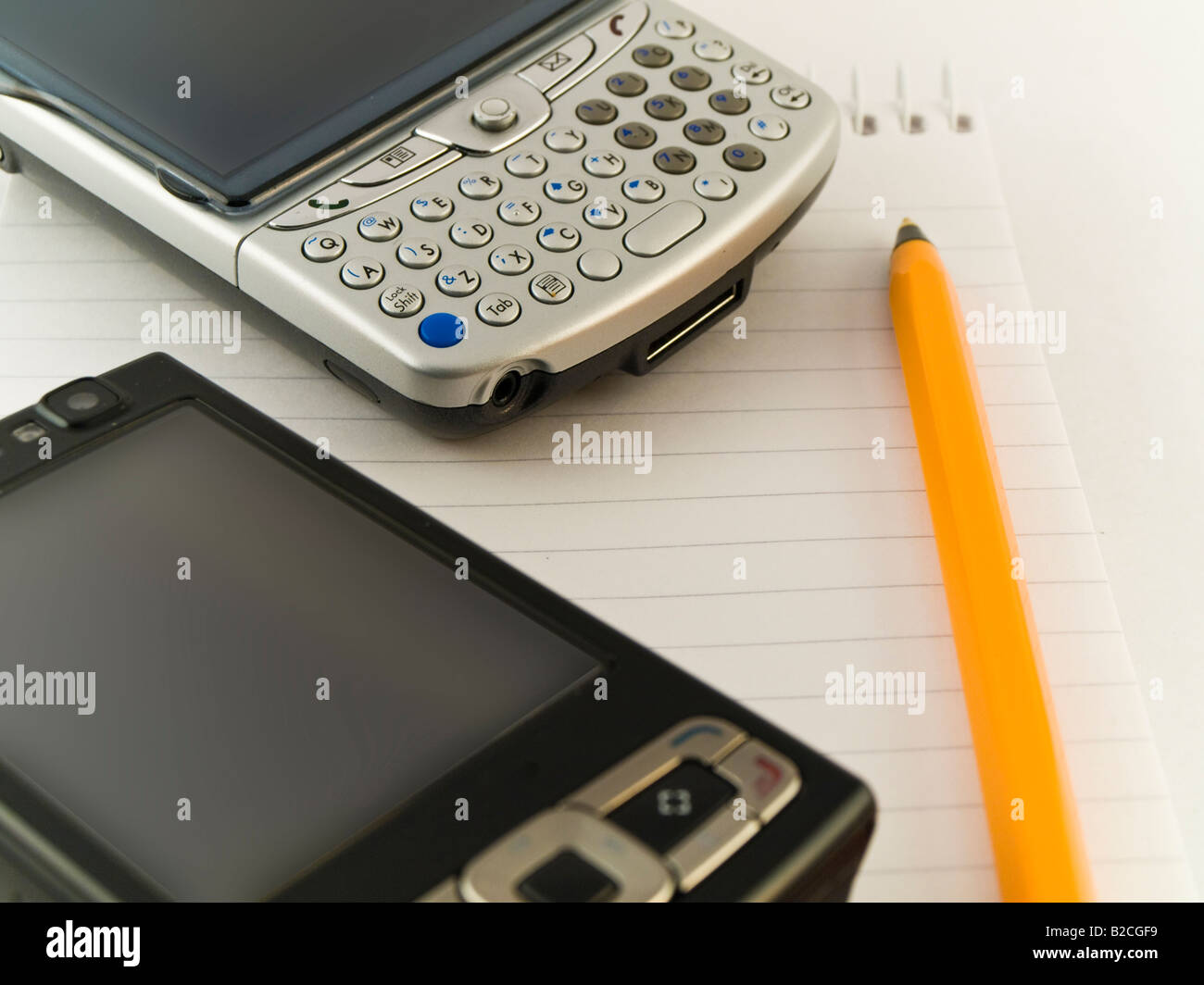Telefoni cellulari e penna su notepad sullo sfondo bianco Foto Stock