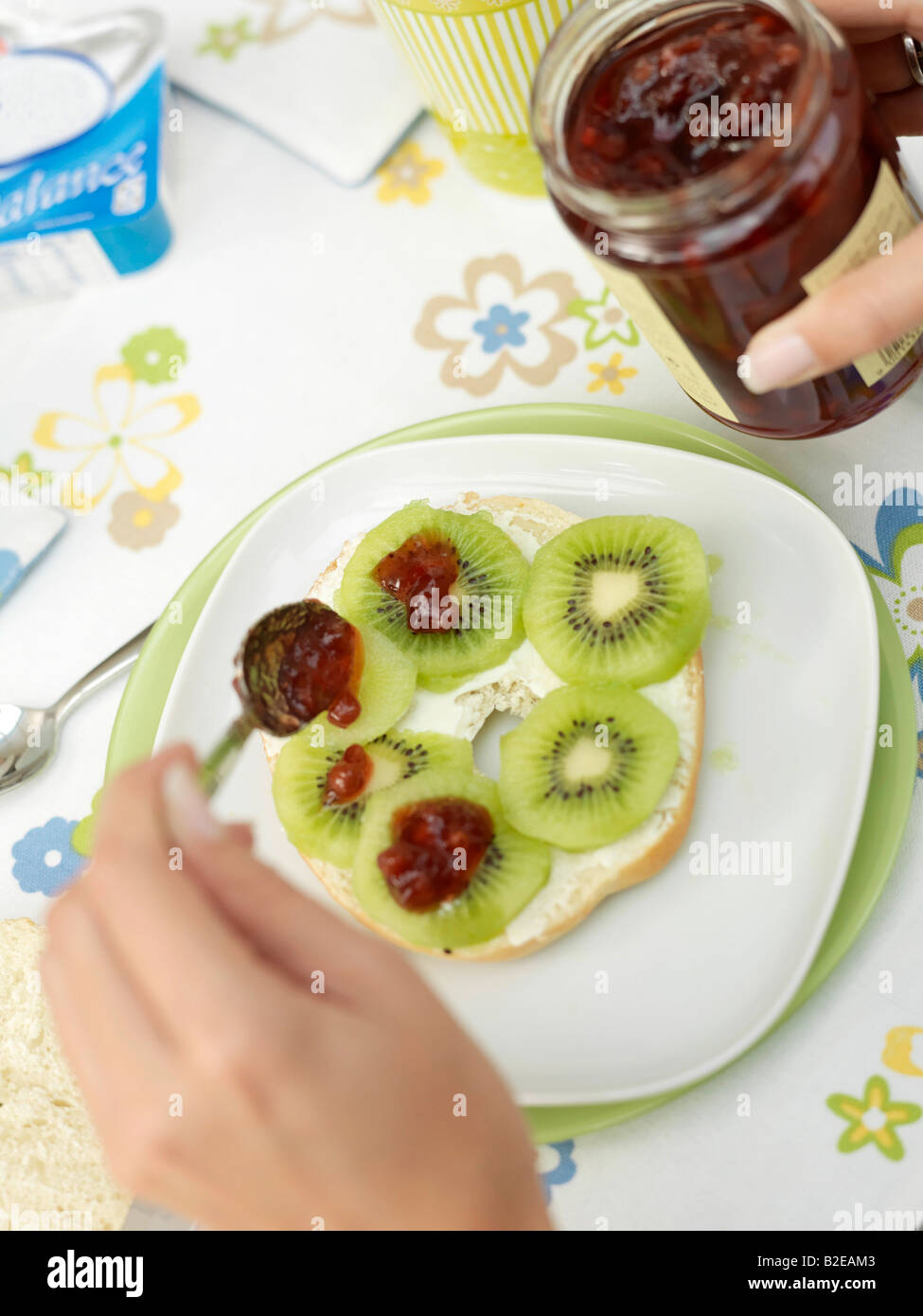 Close-up di persona mettendo mano jam su fette di kiwi Foto Stock