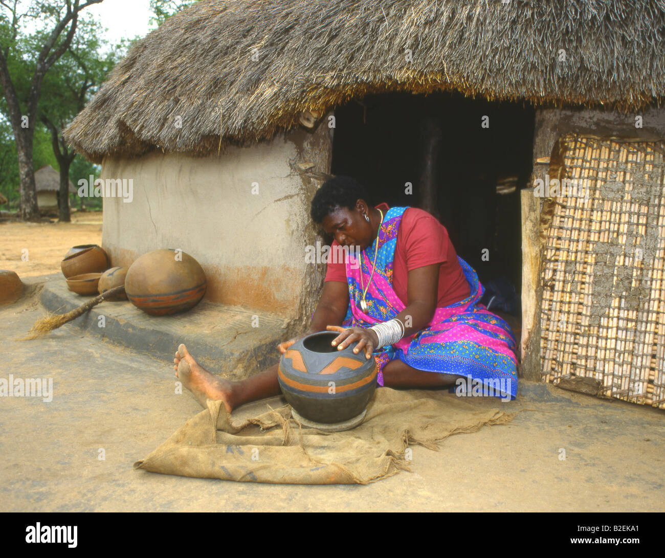 Tsonga donna seduta nel vano della porta di un tradizionale di fango e paglia hut decorare un pot fatti a mano Foto Stock