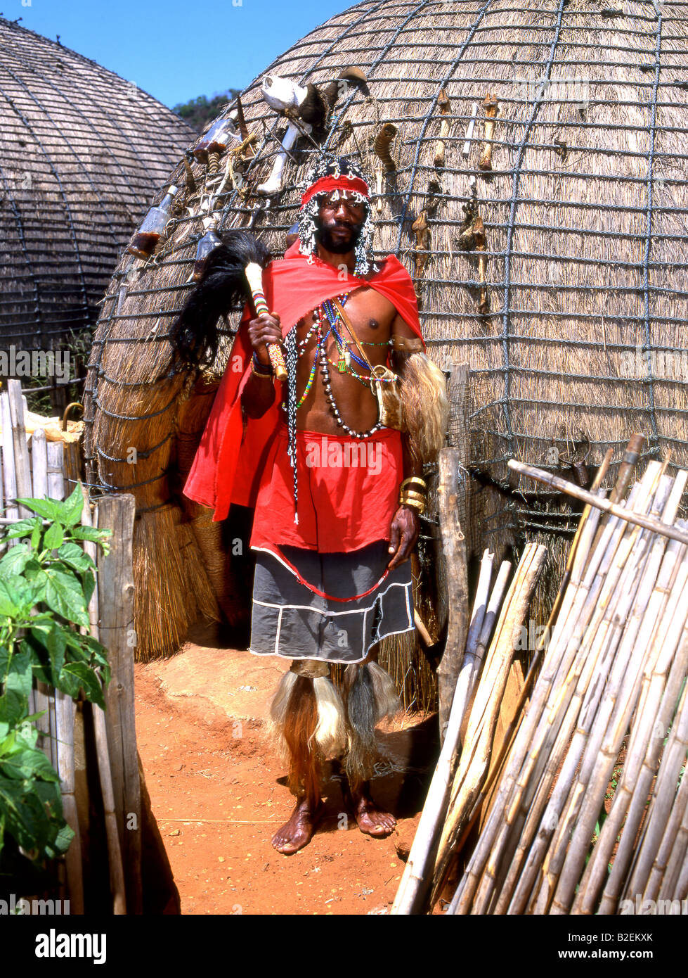 Zulu Sangoma o rabdomante in abito tradizionale di fronte beehive capanne Foto Stock
