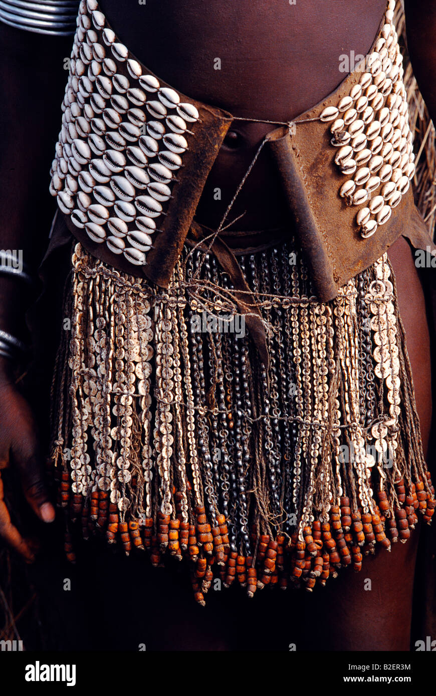 Un Nyangatom donna che indossa un elegante mantello con un breve bordato frangia al font e lunga coda di vitello di raggiungere il suolo. Foto Stock