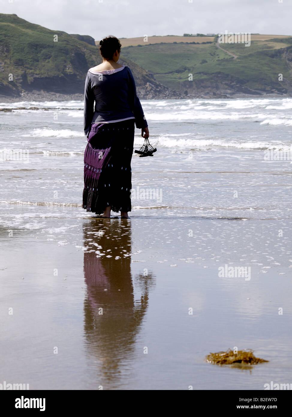 Donna in piedi nel mare con le sue scarpe nelle sue mani da dietro Foto Stock