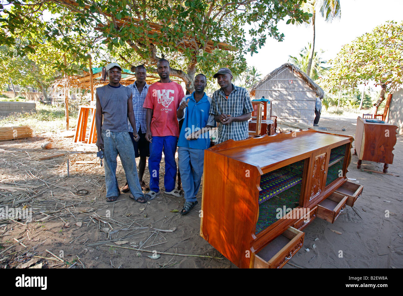 Un gruppo di ebanisti pongono accanto al completamento di un armadio di stoviglie all'aperto, in una fabbrica di mobili nelle zone rurali del Mozambico Foto Stock