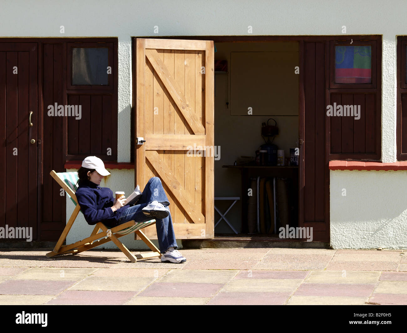 Donna seduto nella sedia a sdraio al di fuori di una capanna sulla spiaggia, a bere caffè e la lettura, Foto Stock