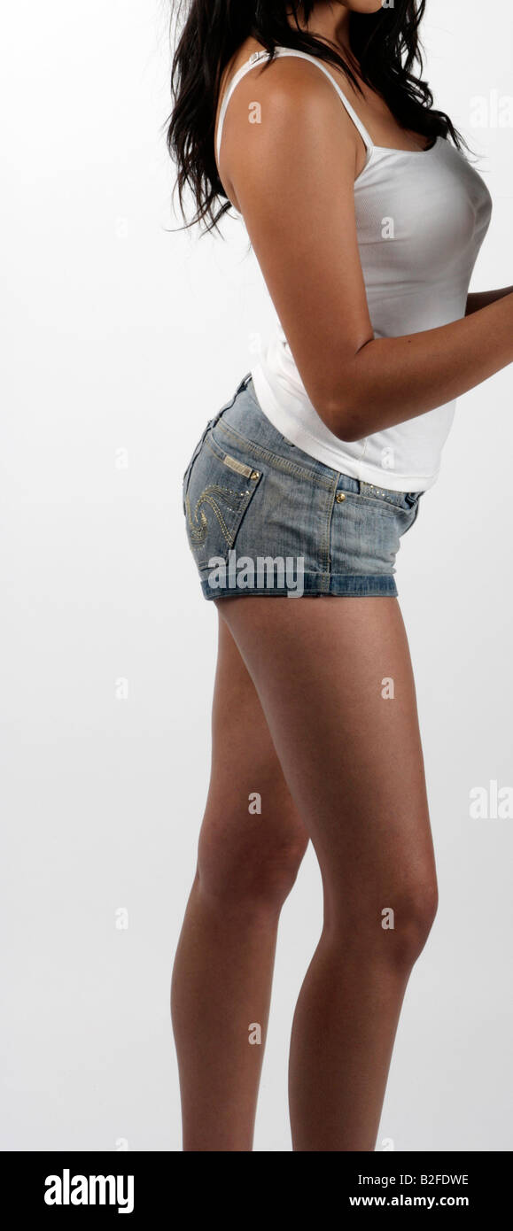 Giovani sinuosa donna africana indossando un bianco strappy top e gli shorts in denim blu afro-caraibica curva voluttuoso marrone della pelle Foto Stock