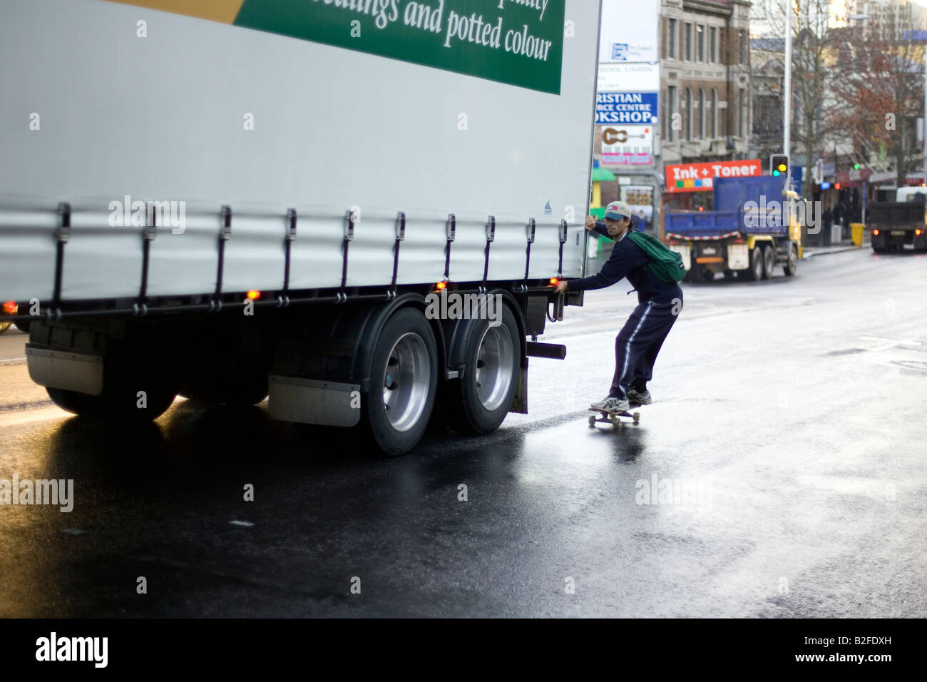 Un guidatore di skateboard appeso su di un carrello in movimento su Queen Street, Auckland Foto Stock
