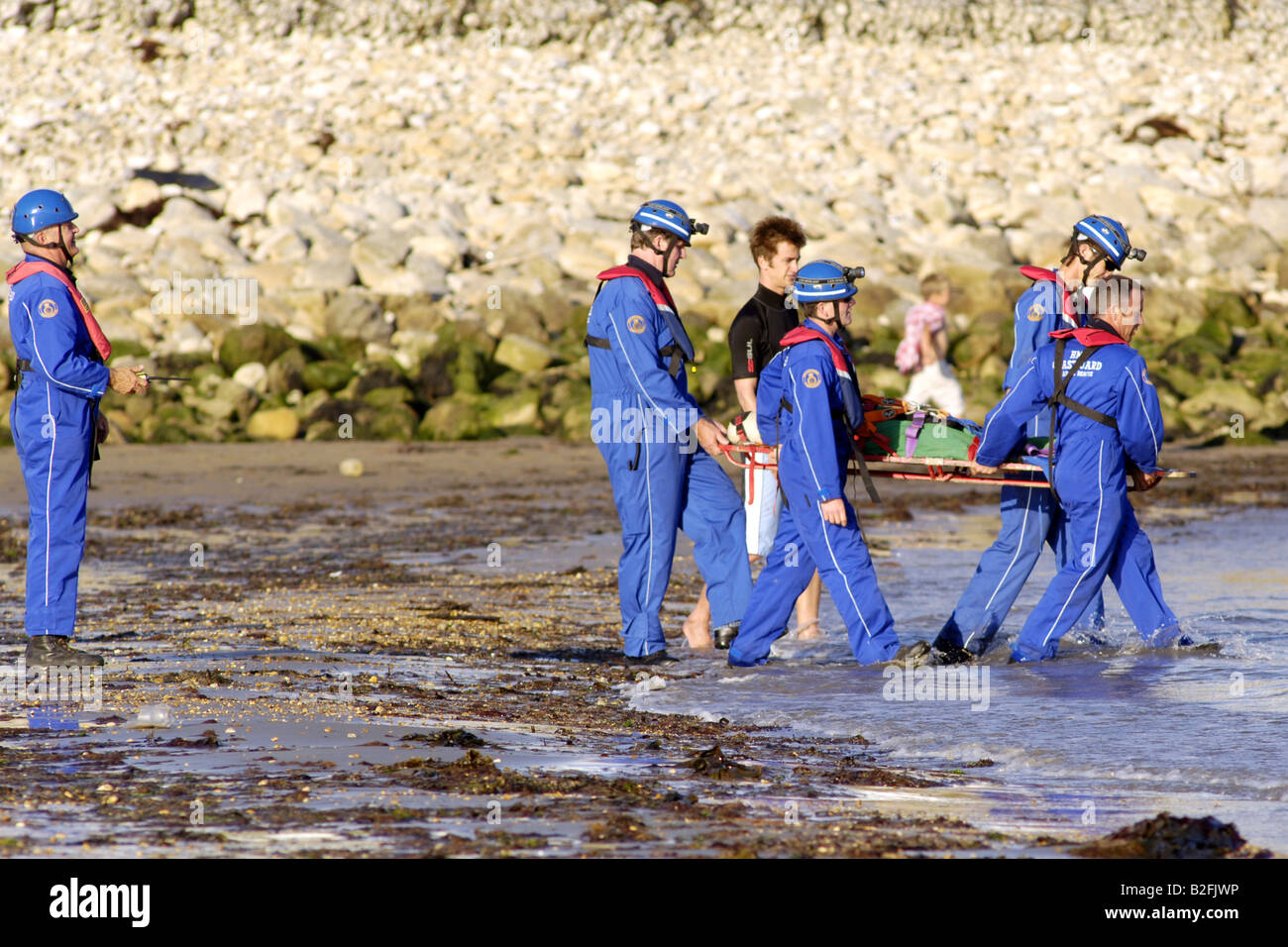 Una guardia costiera sulla riva volontari di soccorso nella sua tute blu da trasportare un corpo ad una scialuppa di salvataggio in attesa Foto Stock