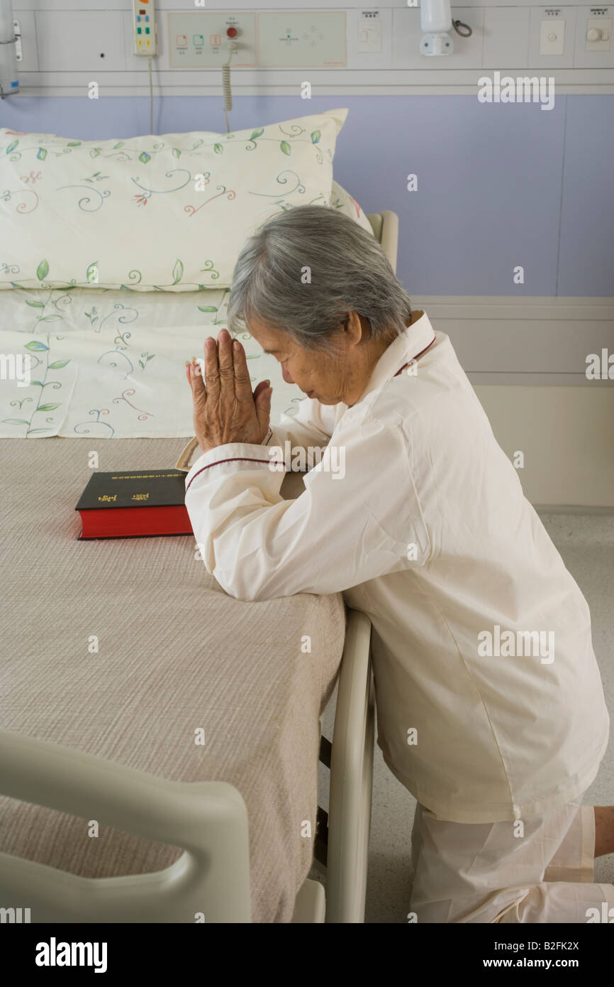 Profilo laterale di un paziente femmina pregando accanto al letto dell'ospedale. Foto Stock