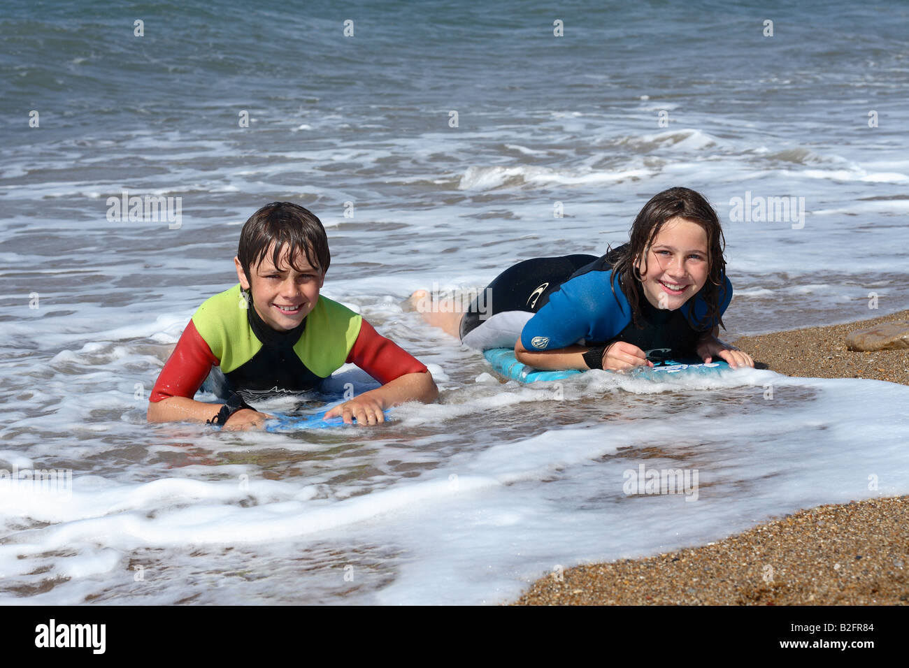 Due figli adolescenti utilizzando schede di corpo nel surf a Burton Bradstock Dorset indossando vestiti bagnati Foto Stock