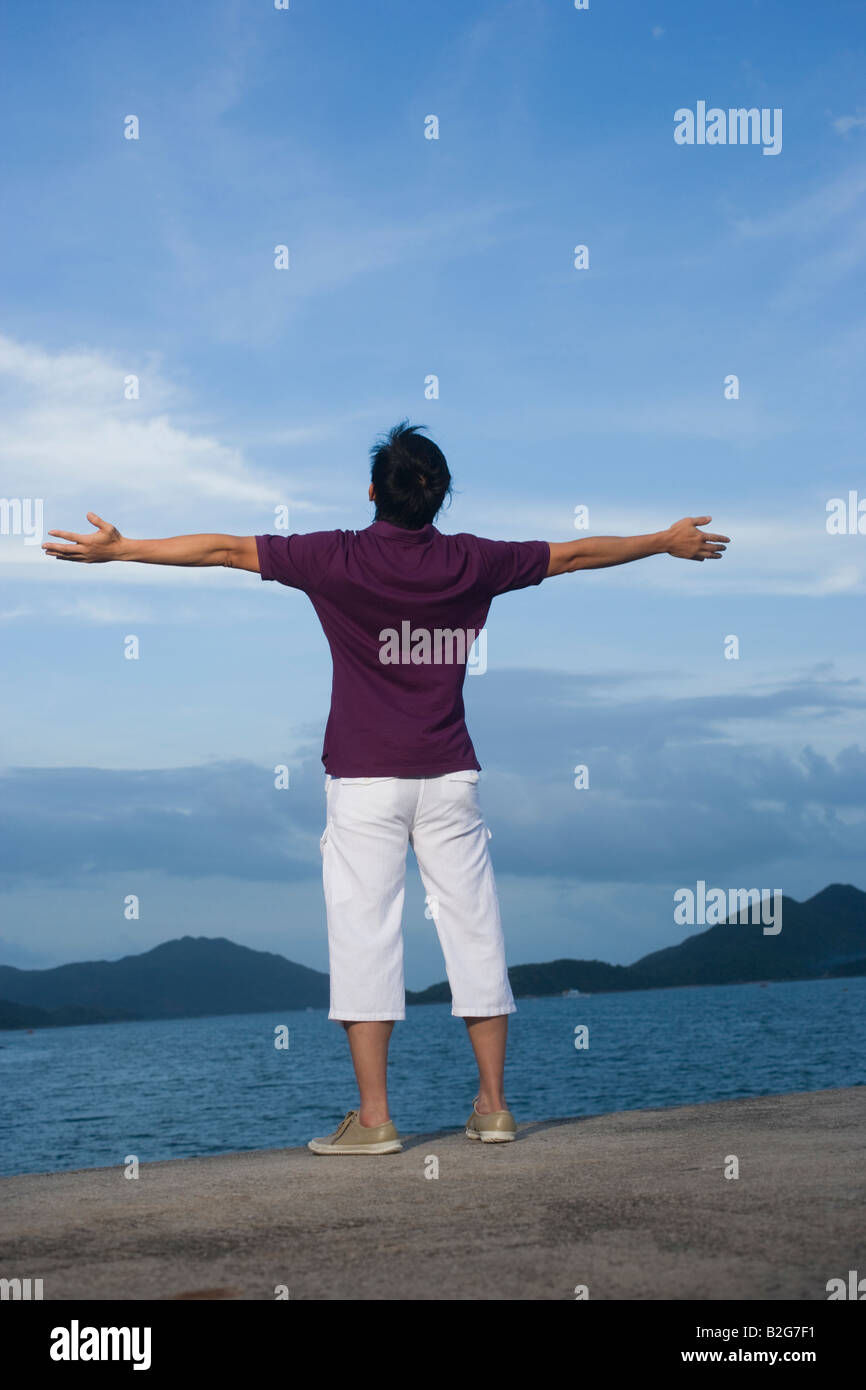 Vista posteriore di una metà uomo adulto permanente sulla spiaggia con braccia aperte Foto Stock