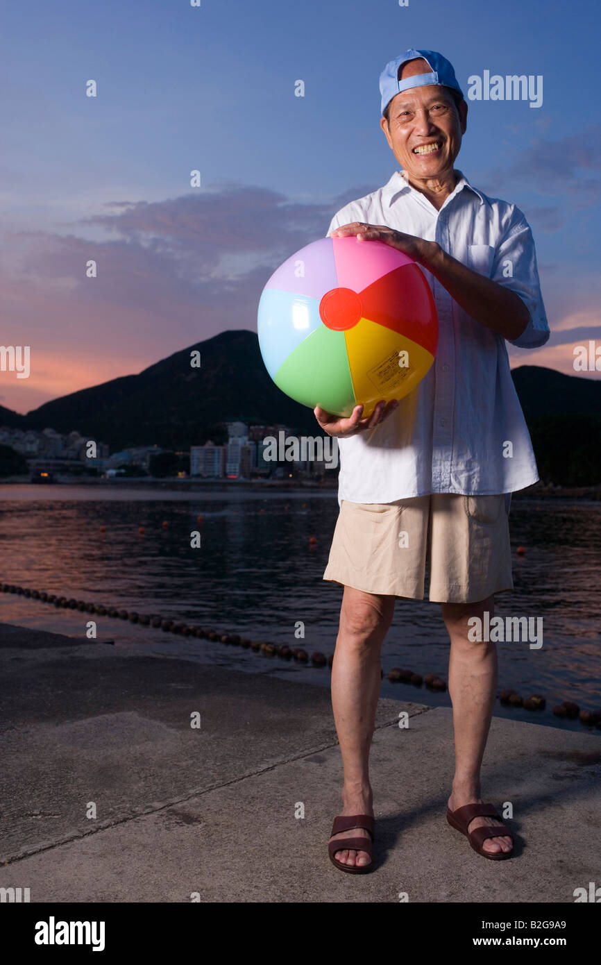 Ritratto di un uomo anziano tenendo una palla spiaggia in riva al mare Foto Stock