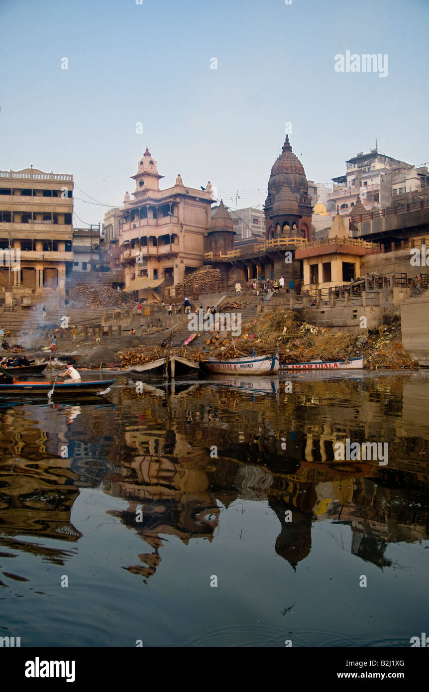 Gli edifici si riflette nel fiume Gange dove aria aperta cremazioni sono eseguite presso l'antica città di Varanasi (India). Foto Stock