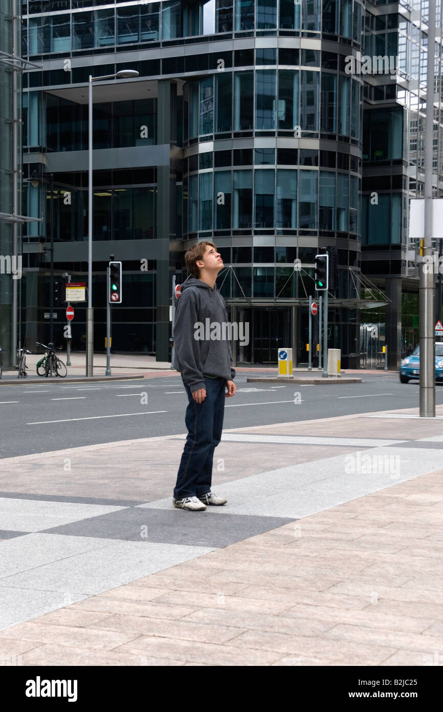 Ragazzo adolescente in piedi sul pavimento in un moderno ambiente urbano osservando gli edifici circostanti in Canary Wharf Londo Foto Stock