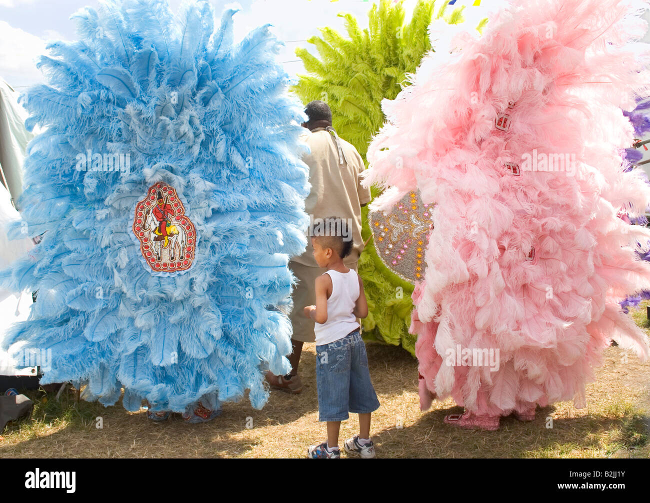 Giovane ragazzo osservando il Mardi Gras costume indiano da dietro. New Orleans Jazz Heritage Festival. Foto Stock
