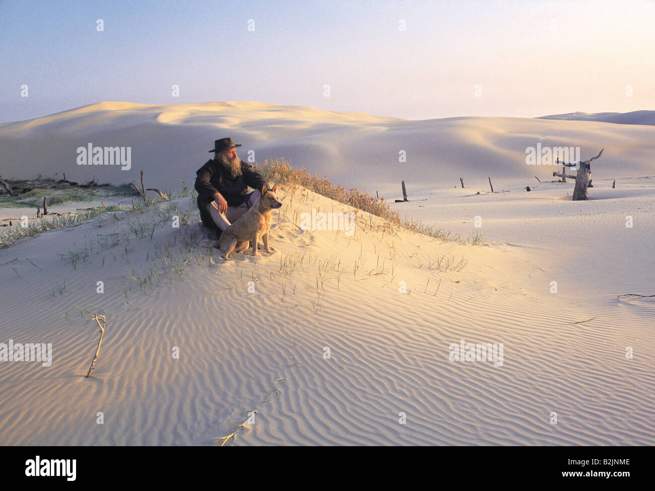 Australia. Outback. Un vecchio uomo con barba grigia seduto con il suo cane sulle dune di sabbia del deserto. Foto Stock