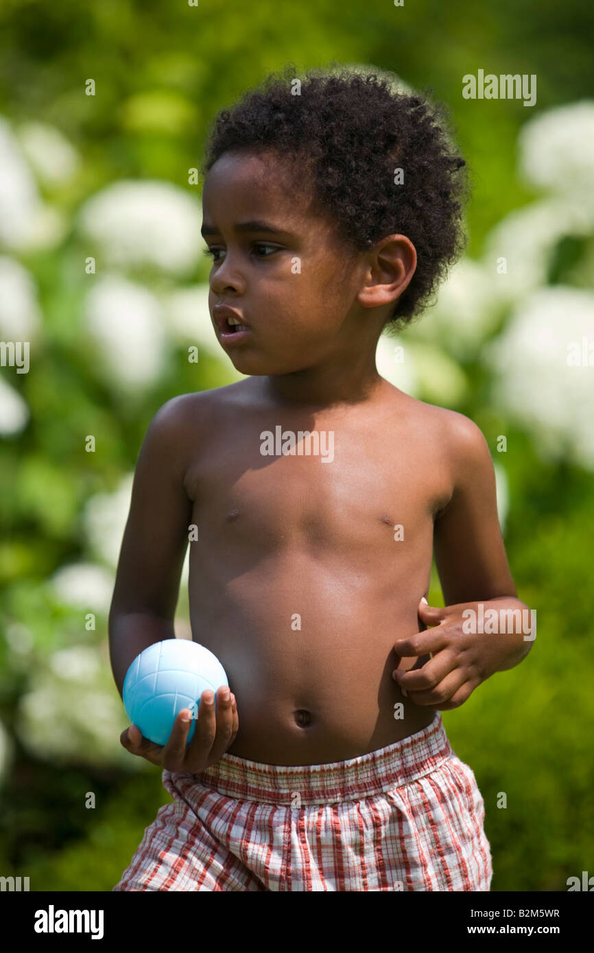 Un ragazzo nero tenendo un blu sfera in plastica. Petit garçon de couleur tenant une boule de petanque en plastique. Foto Stock