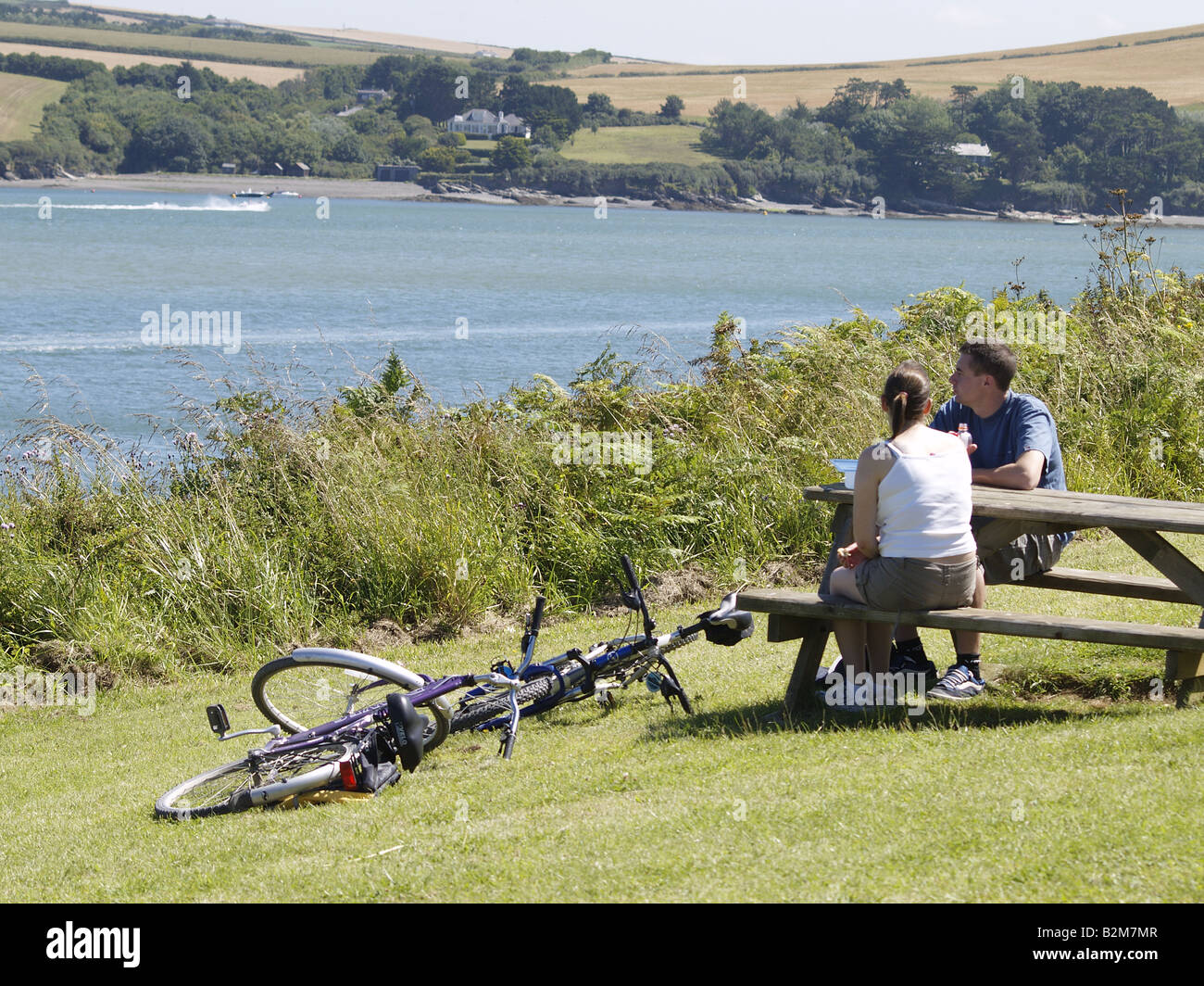 Coppia giovane di ciclisti in appoggio al tavolo da picnic lungo la costa sud-ovest, per mangiare il pranzo e guardare la vista estuario del cammello Foto Stock