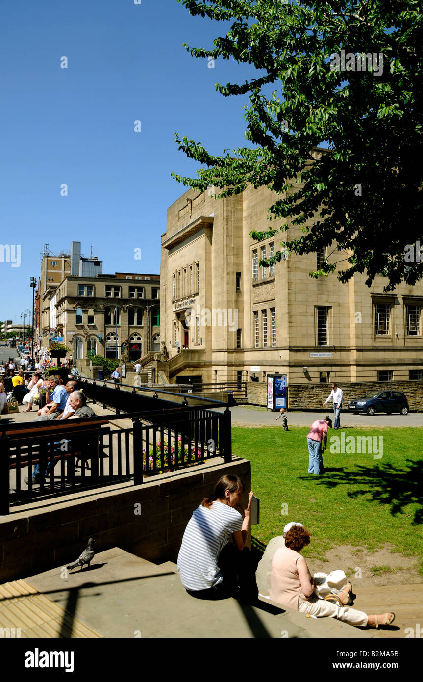 Ora di pranzo gli acquirenti e i lavoratori rilassante sui prati della Piazza Shopping Centre e Biblioteca passi a Huddersfield Foto Stock