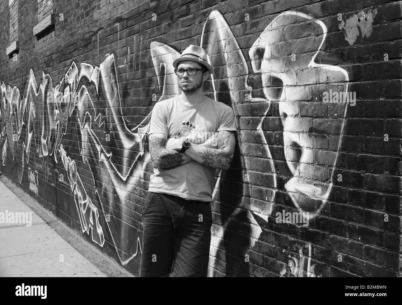 Un giovane maschio caucasico con il corpo di tatuaggi di fronte a un muro di mattoni coperto di graffiti. Un simbolo della gioventù, la vita e la forza. Foto Stock