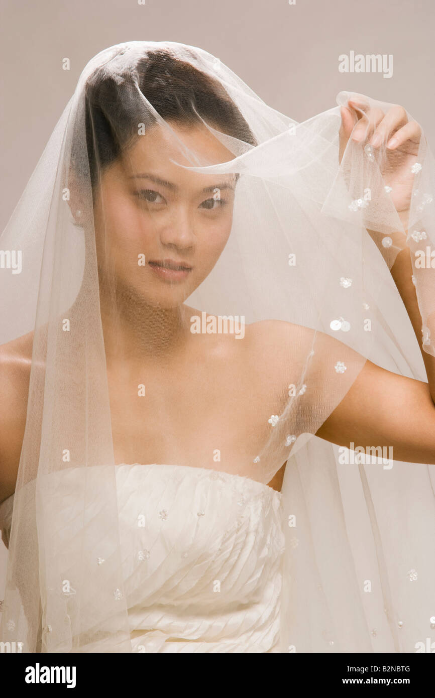 Ritratto di una sposa che copre il volto con un velo e sorridente Foto Stock