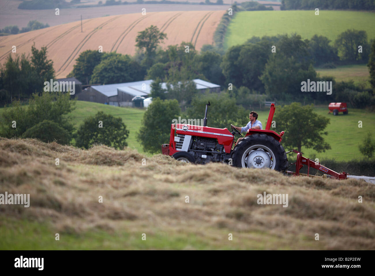 agricoltore seduto su un vecchio trattore massey ferguson 185 che tira un accessorio haymaker in un campo che fa la contea di fieno lungo l'irlanda del nord Foto Stock