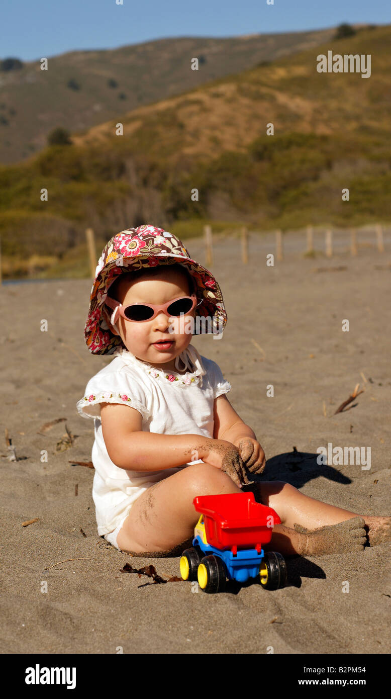 Un neonato ragazza in occhiali da sole illuminato dal sole del tardo  pomeriggio gioca con la sabbia con un giocattolo carrello Foto stock - Alamy