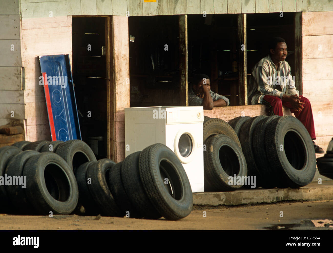 Negoziante seduta sul negozio di fronte con pneumatici usati e lavatrice,  Malawi, Africa Foto stock - Alamy
