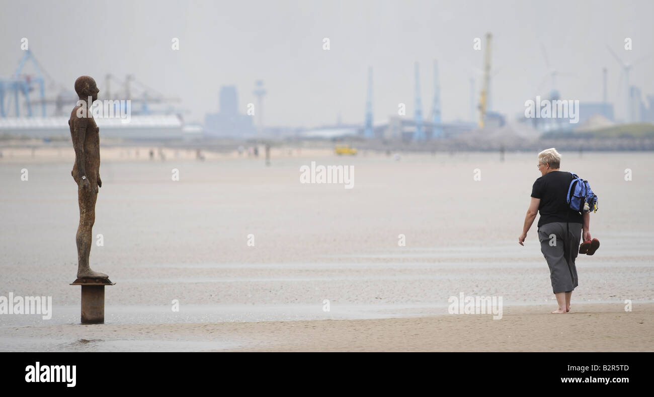 Un viandante guarda a uno degli uomini di ferro statue in Crosby spiaggia vicino Liverpool creato dall'artista Antony Gormley,UK,Inghilterra. Foto Stock