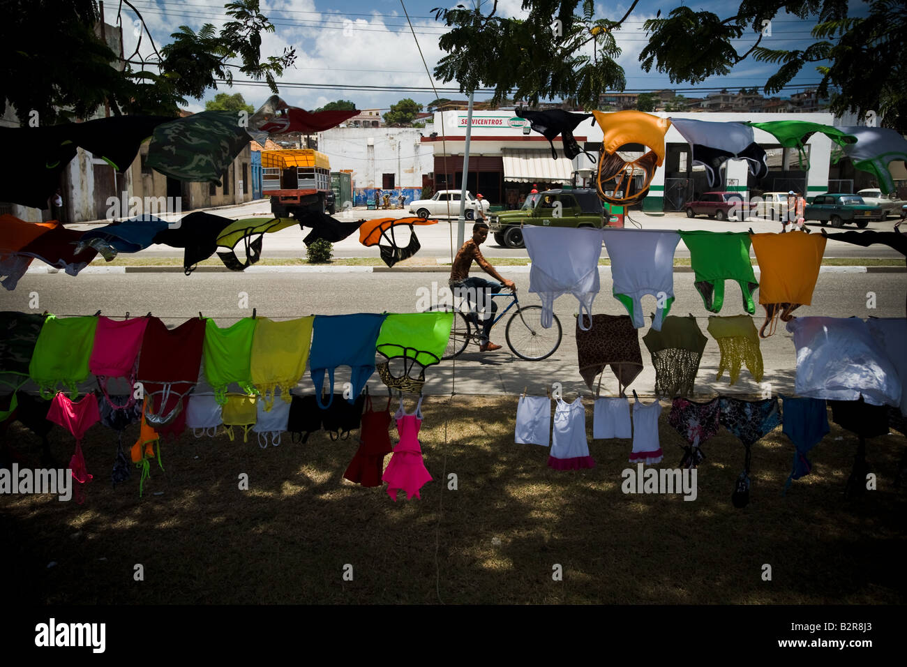 Un ragazzo corse una bicicletta passato le donne gli abiti appesi sulle linee in cui sono offerti in vendita in Santiago di Cuba Foto Stock