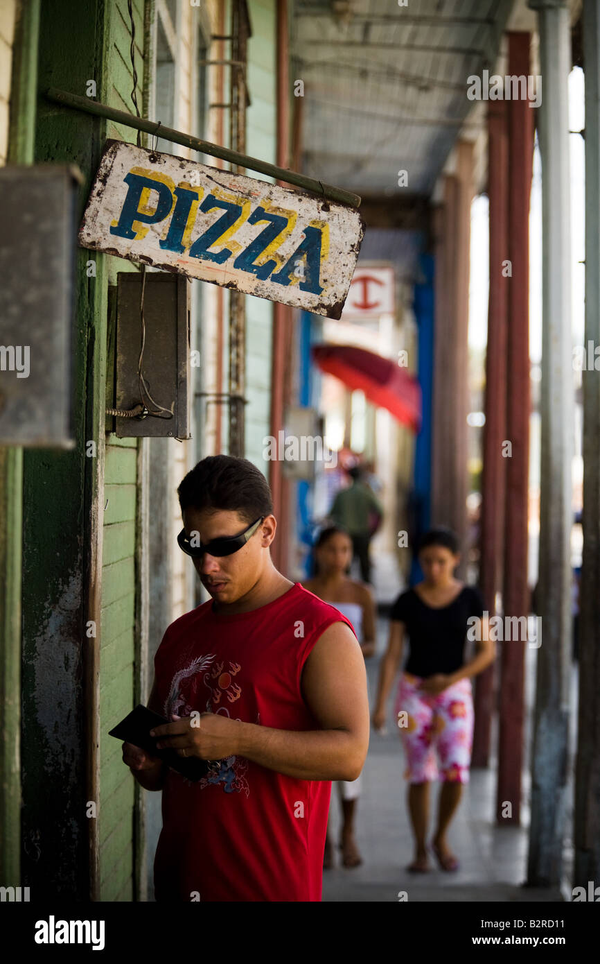 Un uomo rimescola attraverso il suo portafoglio come egli si prepara a pagare per pizza sulla strada di Baracoa, Cuba Foto Stock