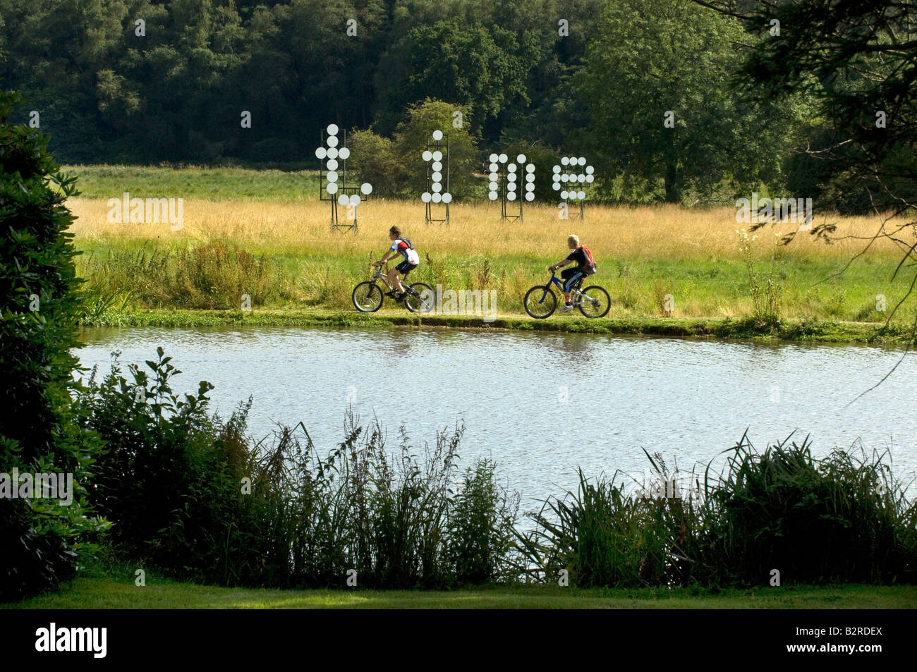 Due boy ciclisti corsa giù per una riva di un fiume passato scultore Jonathan Parsons' installazione di giant floating dot matrix tempo di lettere Foto Stock