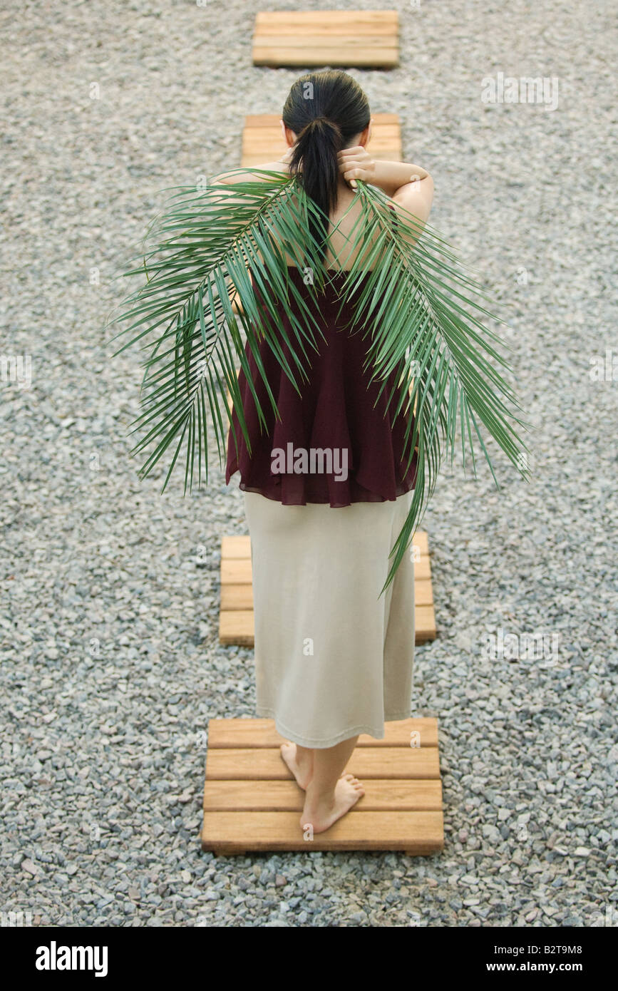 Donna in piedi su foothpath, portanti foglie di palmo dietro la schiena, vista posteriore Foto Stock