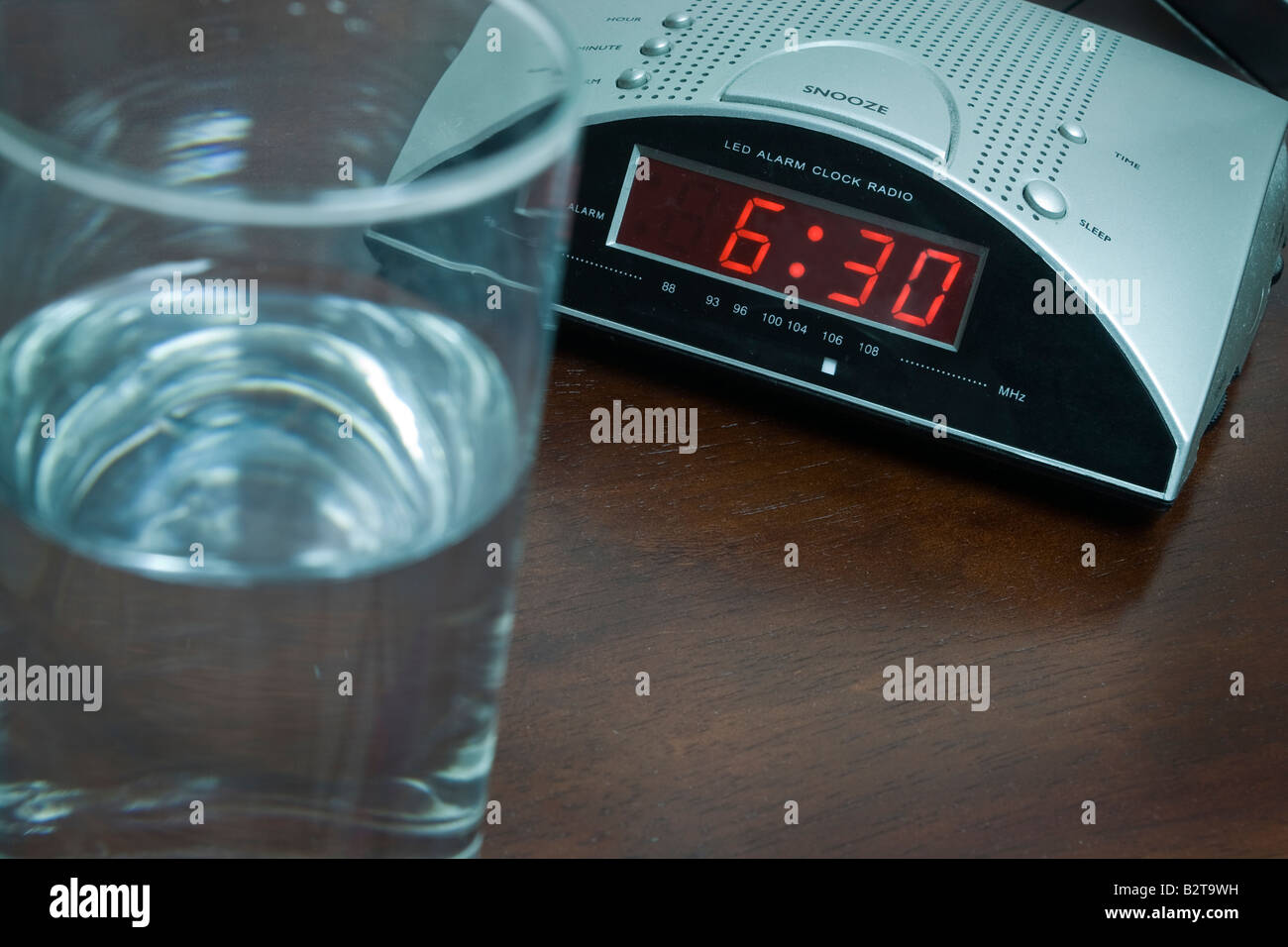 Sveglia alle 6 30 e bicchiere di acqua sul tavolo Foto Stock