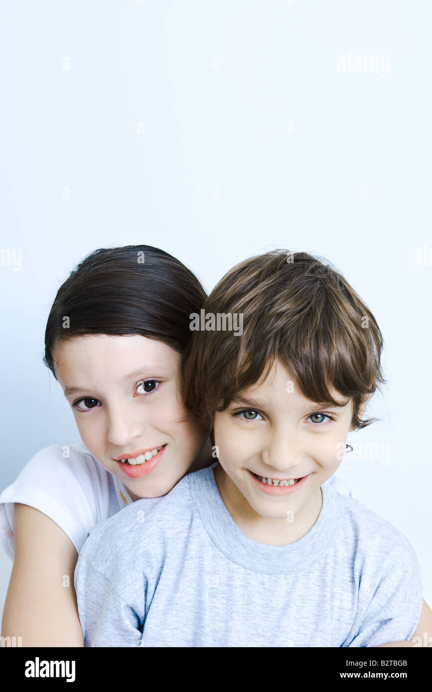Suor abbracciando il fratello da dietro, sorridente in telecamera, ritratto Foto Stock