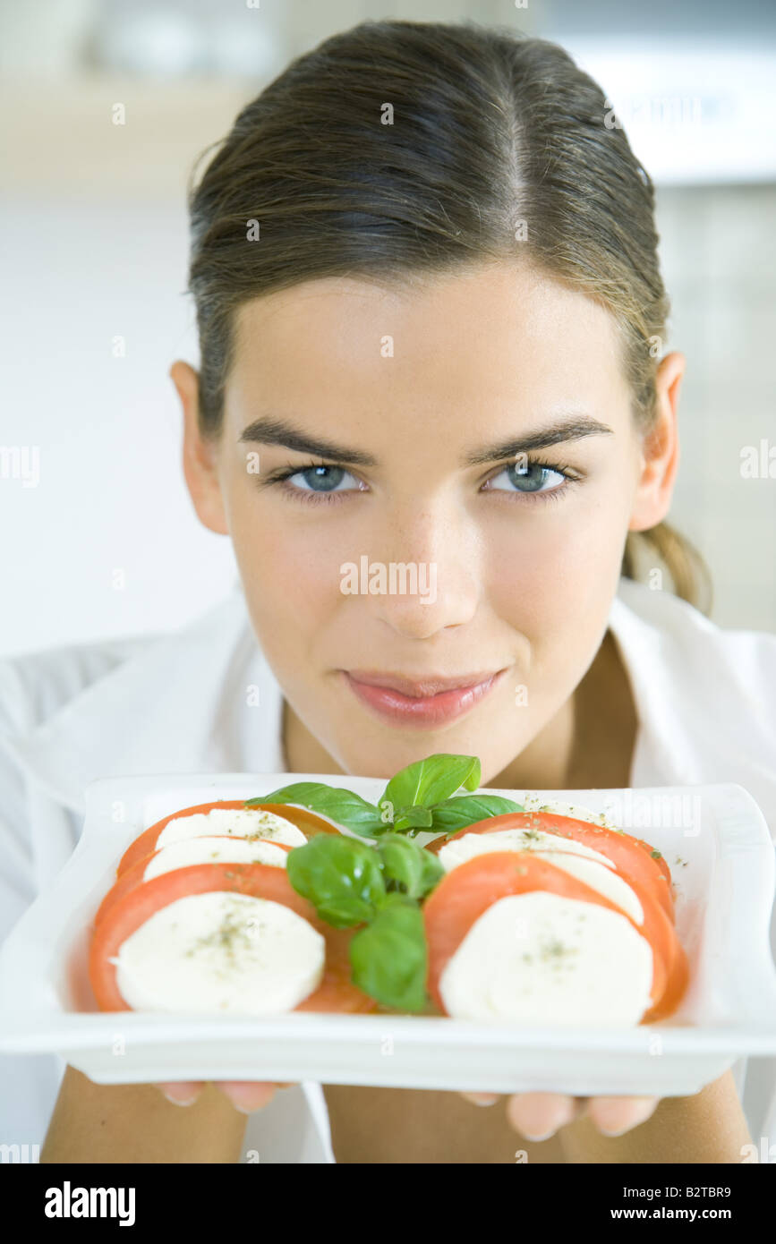 Giovane donna tenendo su un piatto di insalata di pomodoro e mozzarella, sorridente in telecamera Foto Stock